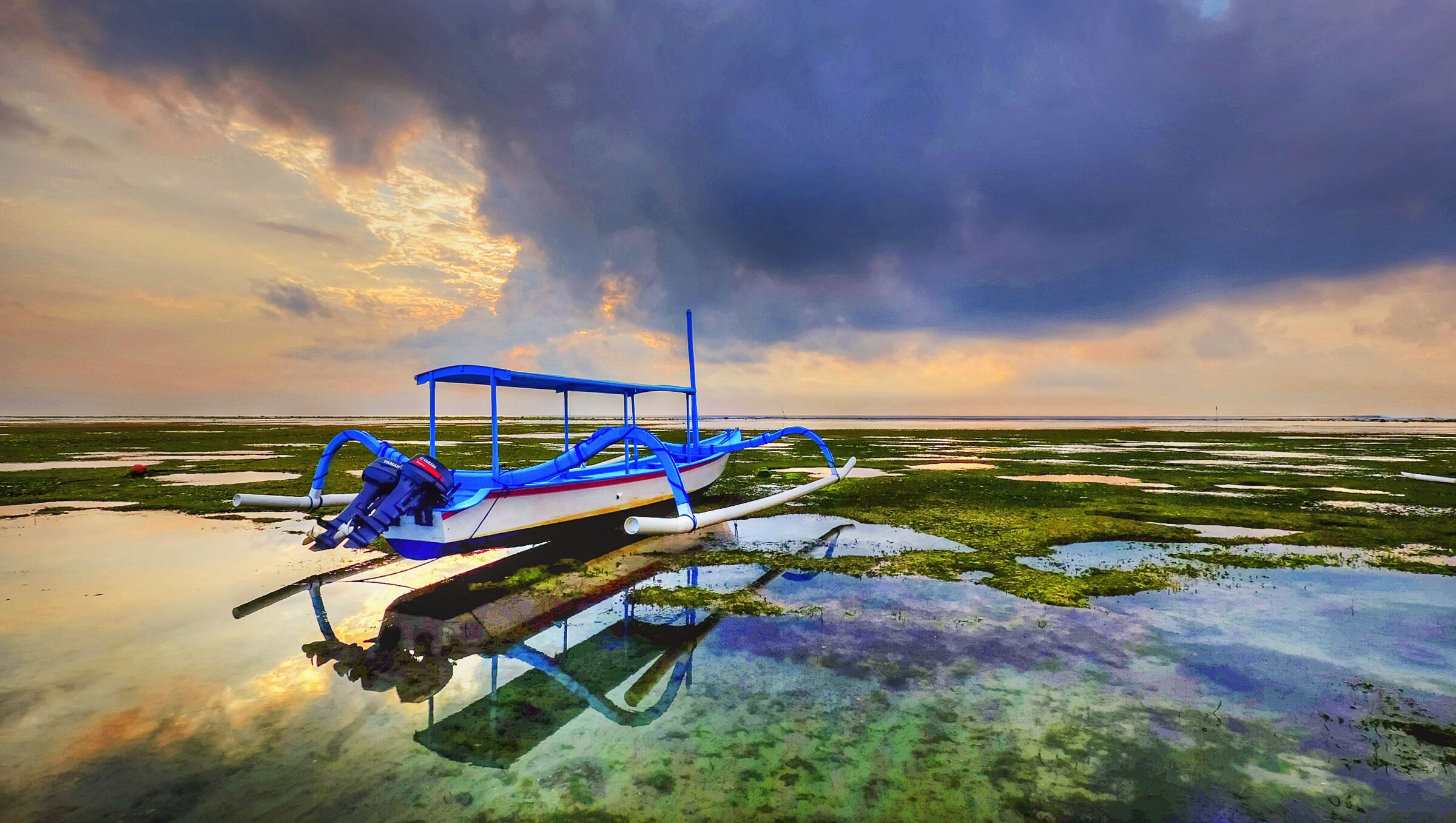 Traditional jukung boat on the tidal flats at low tide under a dramatic dawn sky