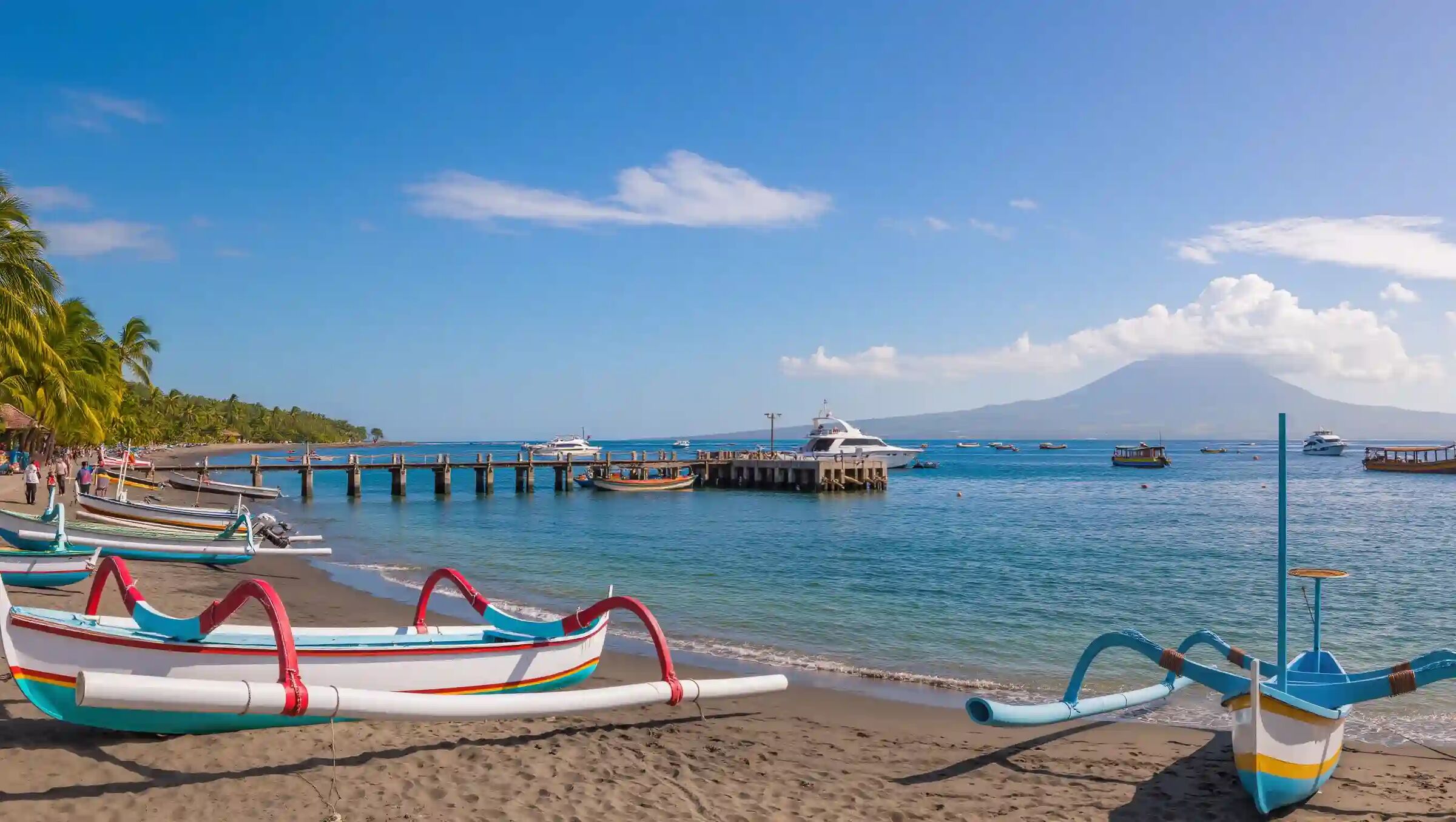 Colourful jukung boats drawn up on Sanur beach beside the boat pier, with Mount Agung on the horizon