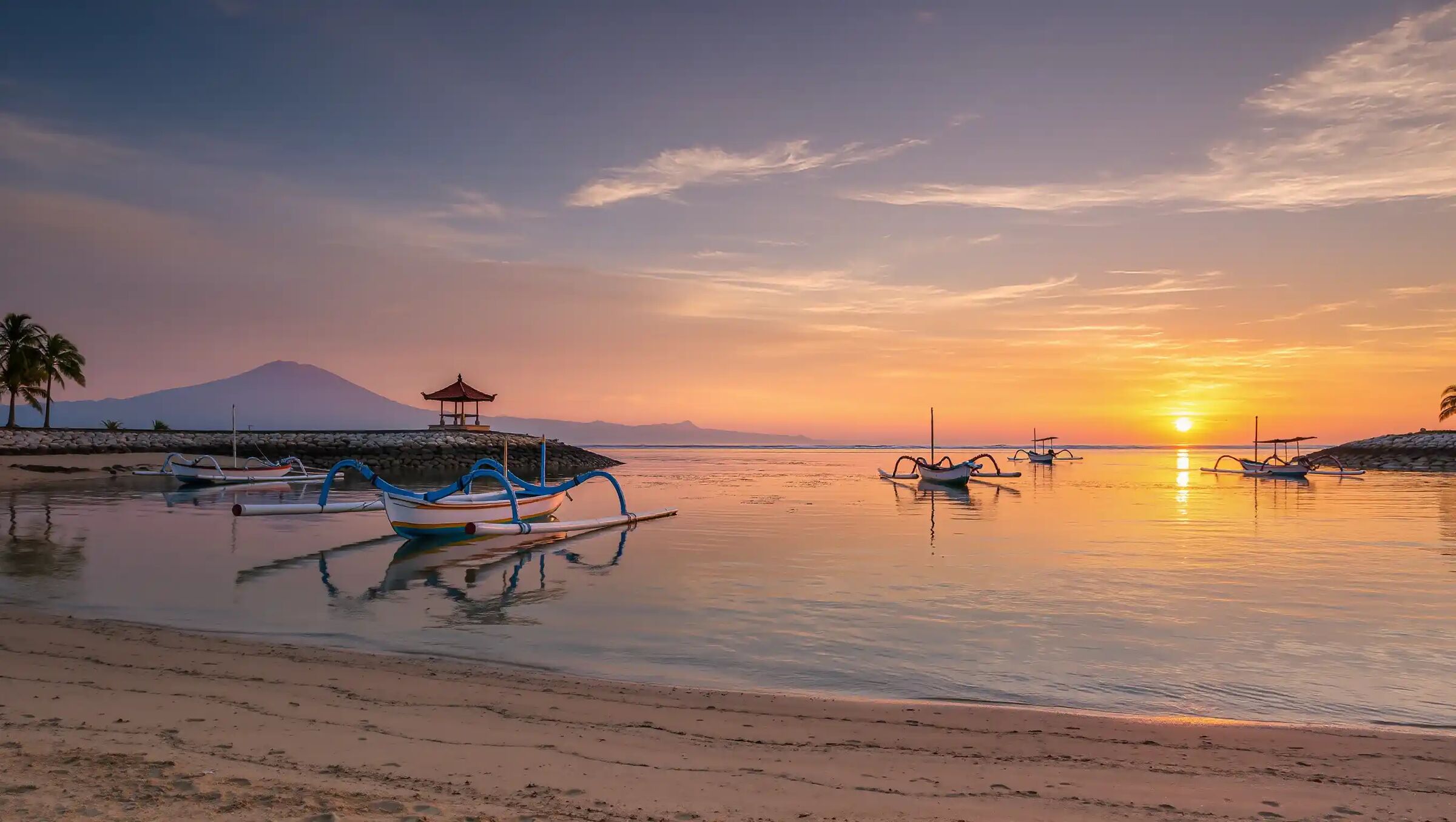 Sunrise over traditional jukung outrigger boats moored off the Sanur coast, the shoreline facing Serangan Island